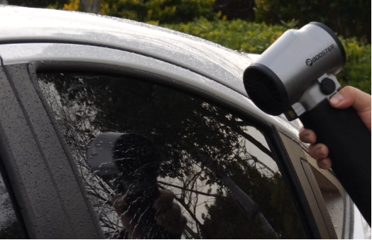 Handheld cordless blower aimed at a water-beaded car side window for drying after a wash.